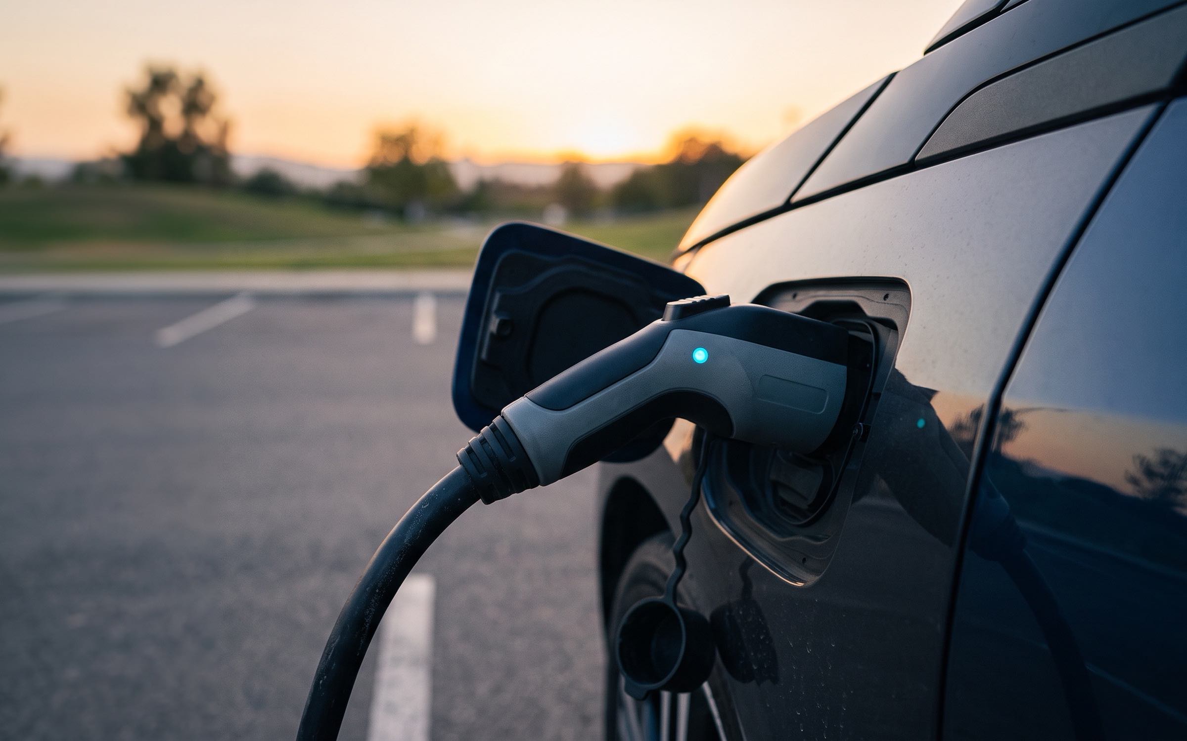 Cable de carga conectado a un coche eléctrico en un parqueadero al atardecer